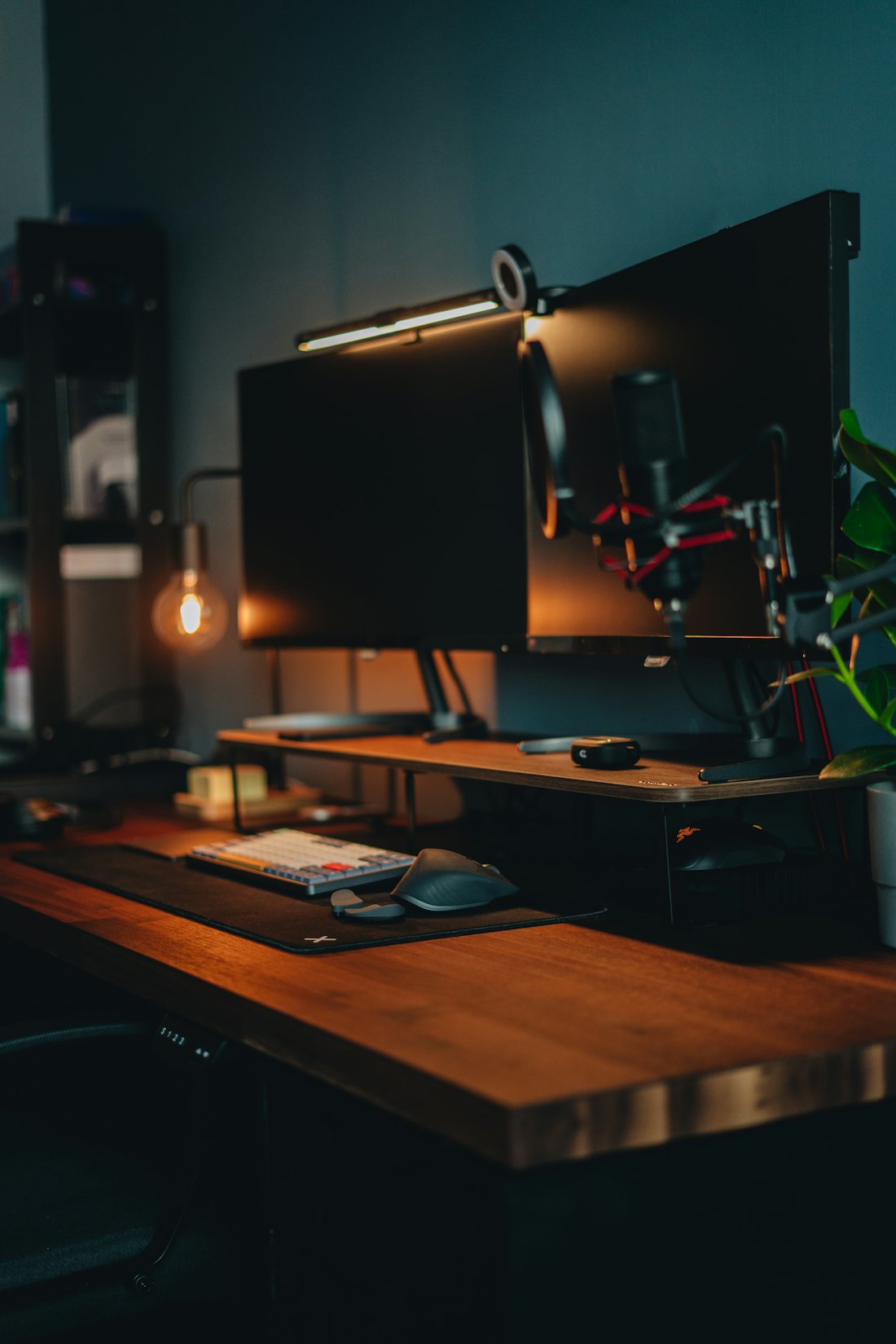 A warm-lit dark desk with a monitor and computer equipment.