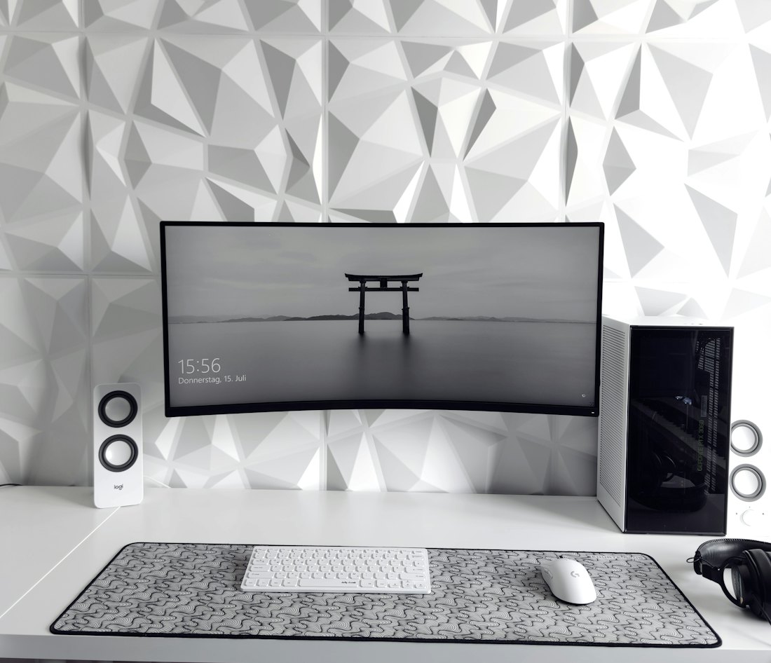 A curved widescreen monitor between two speakers on a white desk.